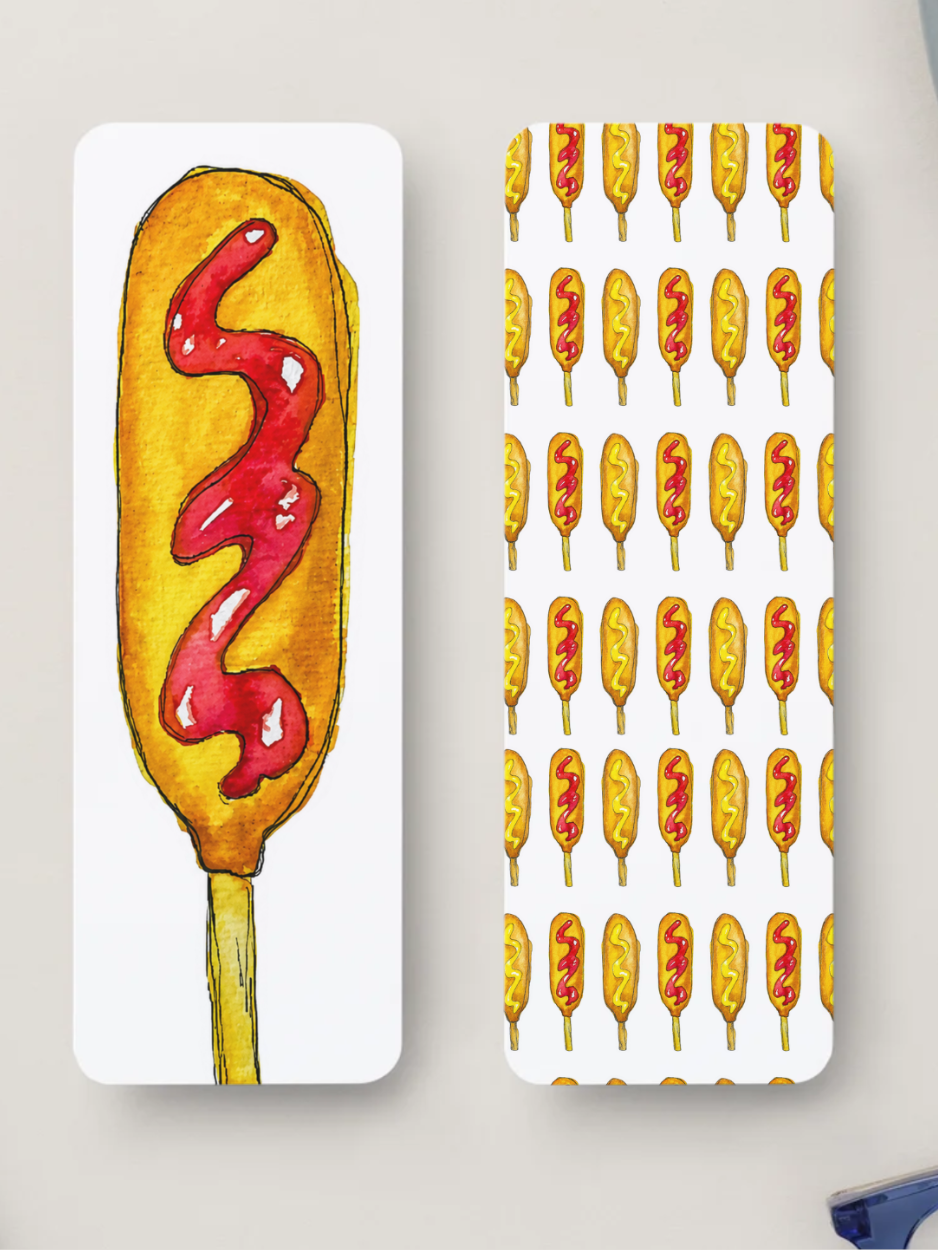 Two bookmarks printed items with rounded corners, shown on a light neutral background. The left item features a large watercolor-style corn dog with red ketchup, and the right item shows a repeating pattern of the same corn dog motif on a white background.