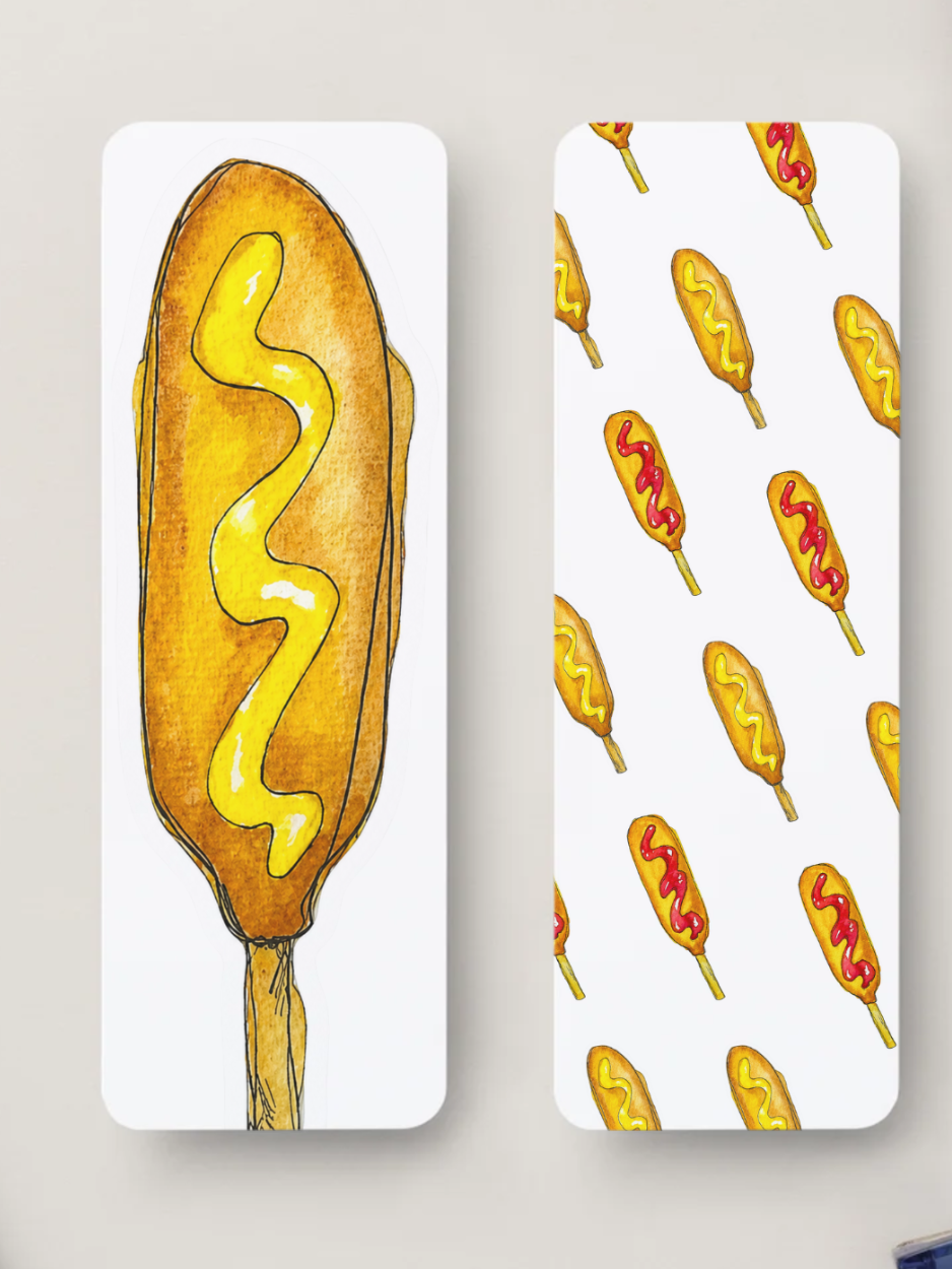 Two bookmarks with rounded corners, shown against a light neutral wall. The left panel features a large hand-drawn corn dog with yellow mustard, and the right panel shows a repeating pattern of smaller corn dogs with mustard and ketchup.