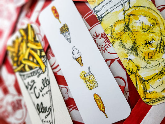 A close-up of several illustrated paper bookmarks laid on top of popcorn bags. The visible designs include Culvers french fries , an ice cream cone, a lemon shake up, and corndogs