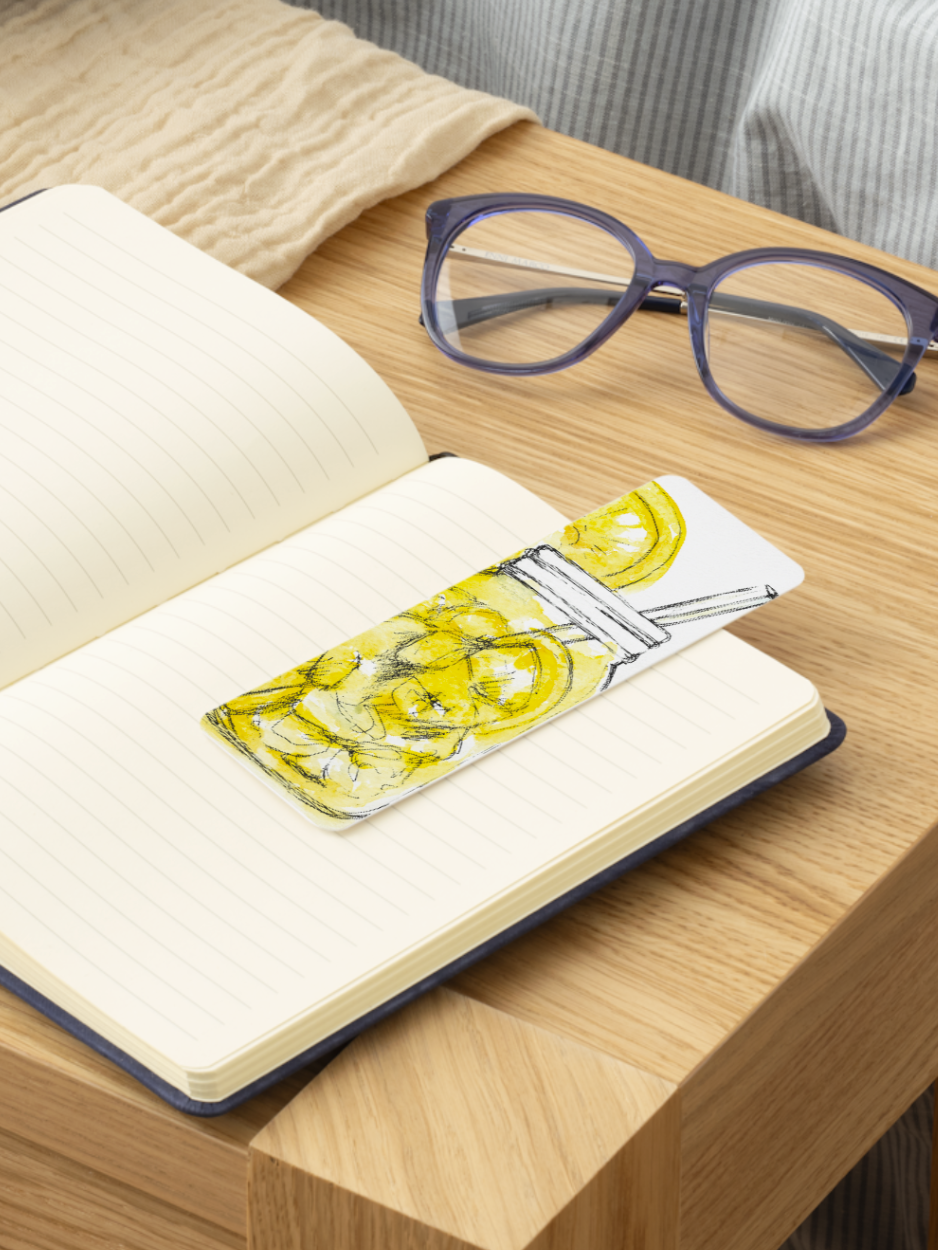Open notebook with a bookmark featuring lemon illustrations on a wooden surface with glasses.