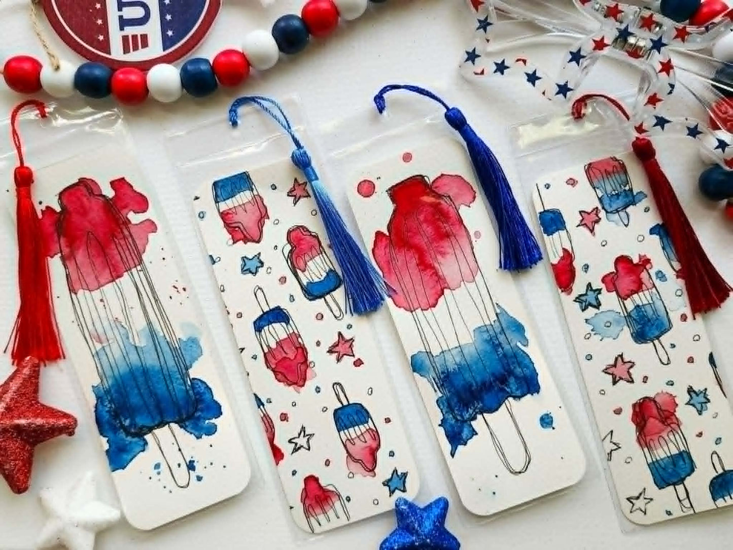 Hand-painted watercolor Bomb Pop bookmark featuring red, white, and blue watercolor splashes with loose black ink details. This patriotic summer bookmark is inspired by classic ice cream truck treats and is printed on textured cardstock for book lovers, teachers, and readers.