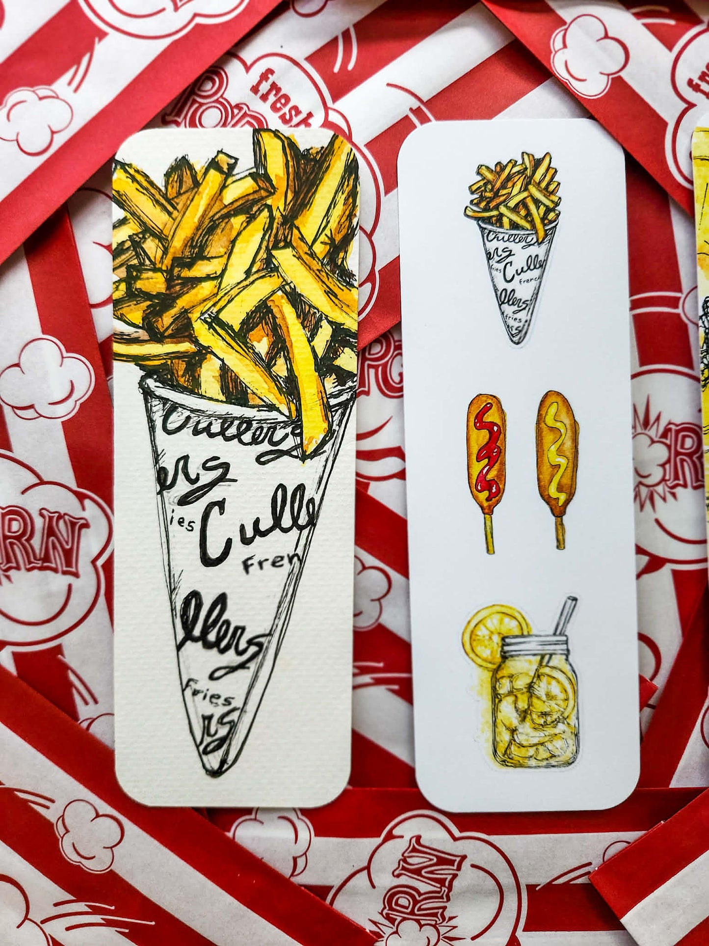 Two white rectangular bookmarks with hand-drawn french fries and food illustrations, placed on red-and-white popcorn bags.